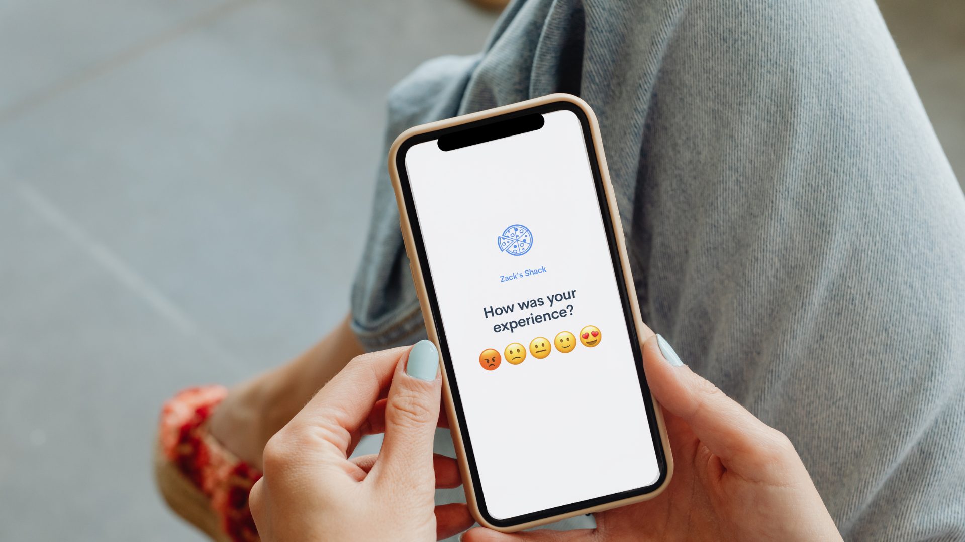 A person looking at their mobile phone which displays a survey asking the guest, "How was your experience"? With five emojis, the restaurant brand name, and the restaurant logo.